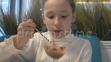 一个穿着白色连衣裙，脸上有雀斑的小女孩坐在咖啡馆里，吃着玻璃杯里的冰淇淋。 从底部看。